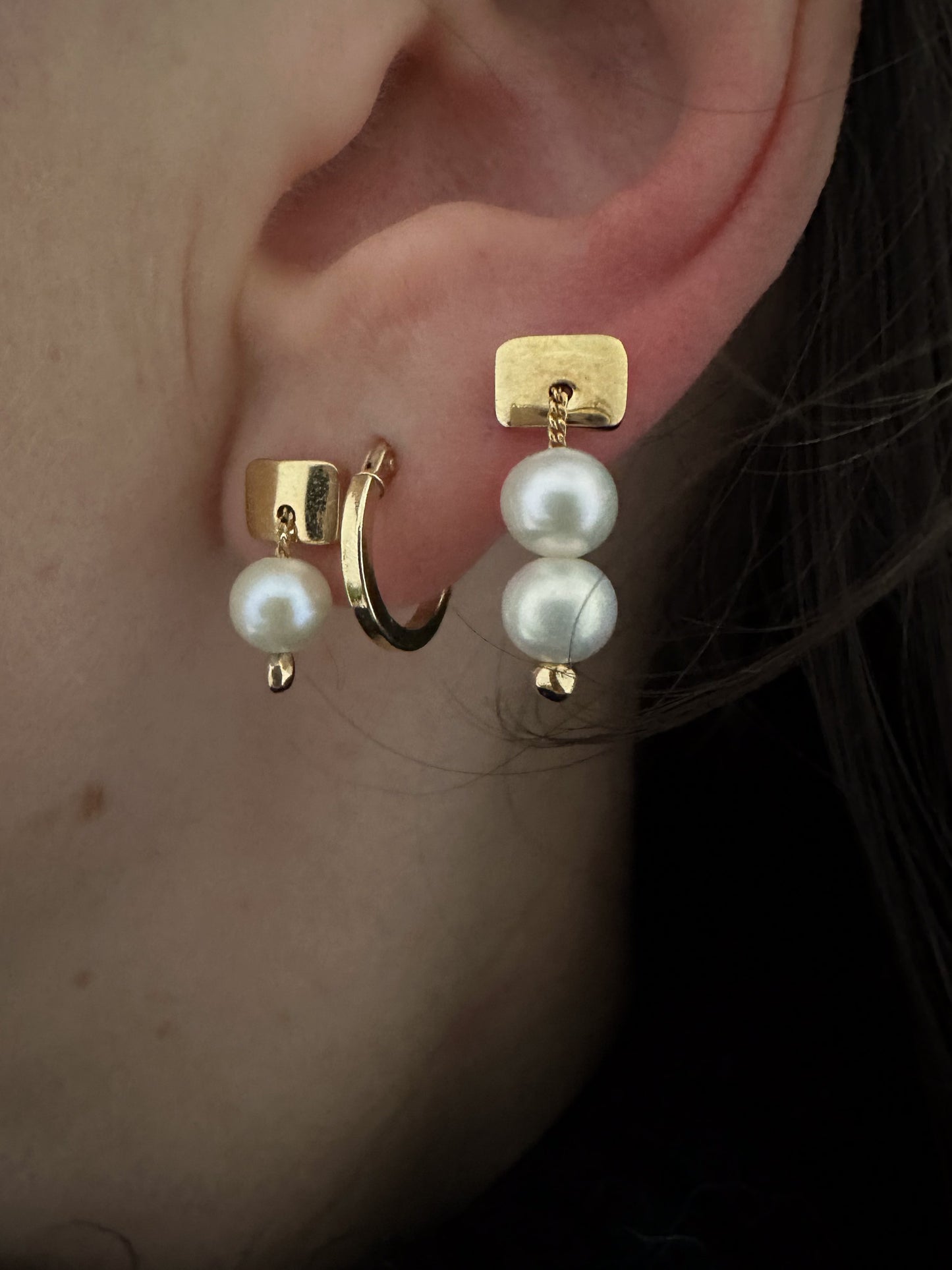 pearl earrings and gold hoop all layered and stacked on an ear.A captivating twist on the timeless solitaire pearl stud design. Single Freshwater Pearl: This exquisite piece showcases a single freshwater pearl, elegantly strung on a sterling silver curb chain and securely affixed to a sterling silver base. Perfectly sized for a subtle earring or for adding to a combination of layered earrings. High-Grade Freshwater Pearl: 6mm round freshwater pearl, chosen for its luminous beauty.