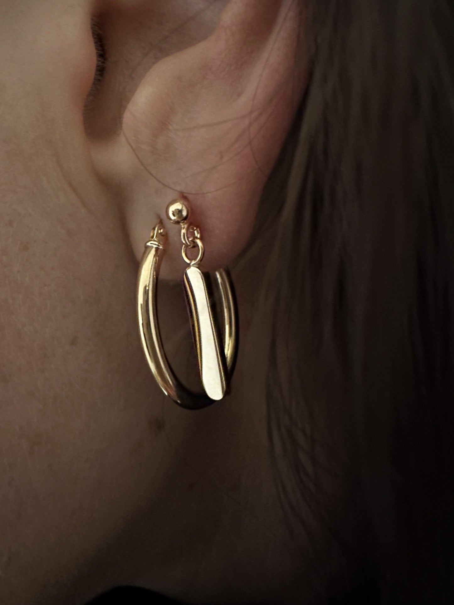 Minimalist dangling earrings. Handmade from 925 sterling silver, these earrings possess a substantial weight that enhances the graceful swing of the product. The weightiness adds to their allure, making them a delightful jewellery choice for any occasion.. Paired here with gold oval hoop earrings.