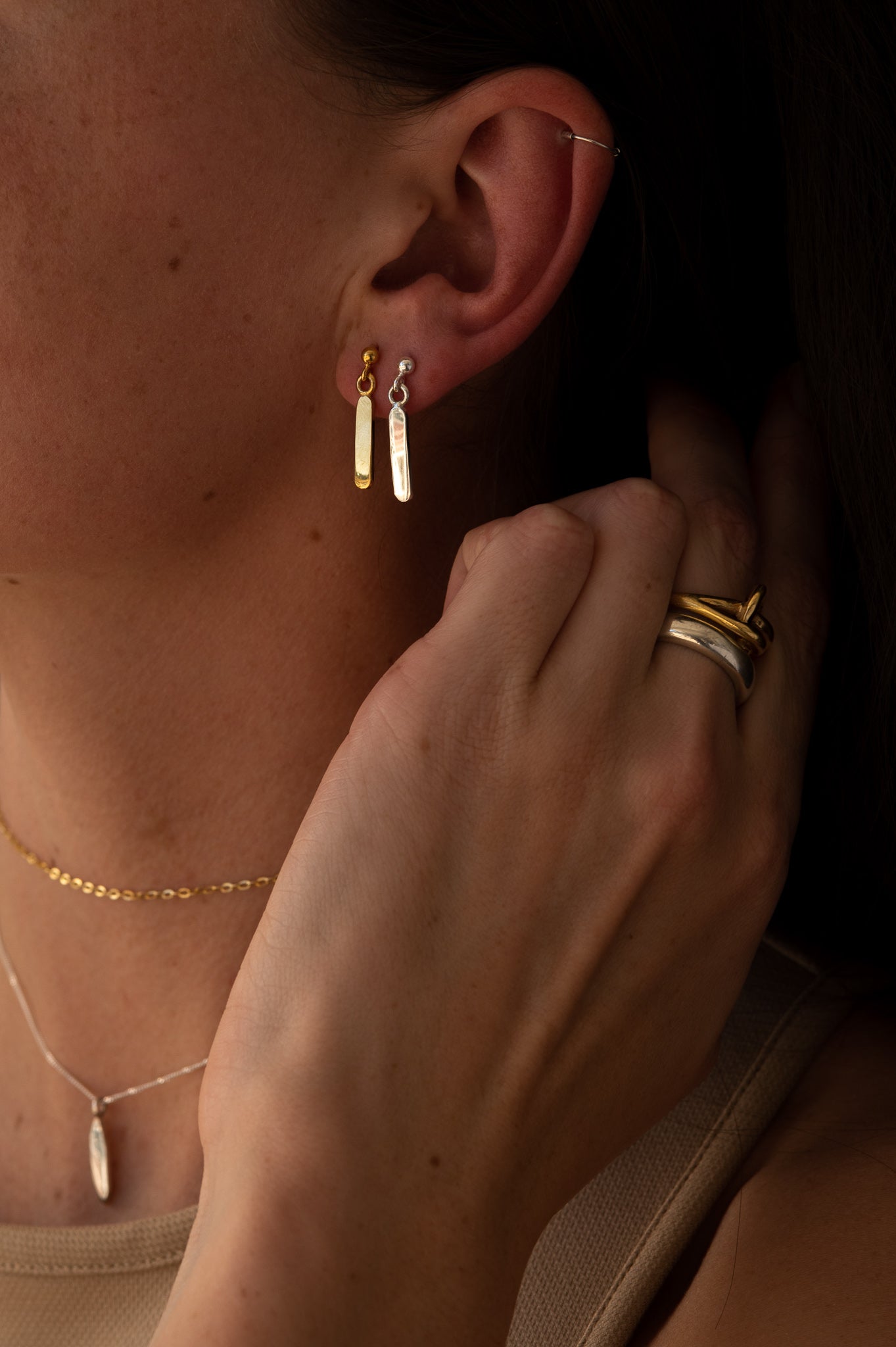 Minimalist dangling earrings. Handmade from 925 sterling silver, these earrings possess a substantial weight that enhances the graceful swing of the product. The weightiness adds to their allure, making them a delightful jewellery choice for any occasion.. model wears two earrings on one ear, on in gold and the other in silver. she pairs it with a solid gold choker chain necklace.