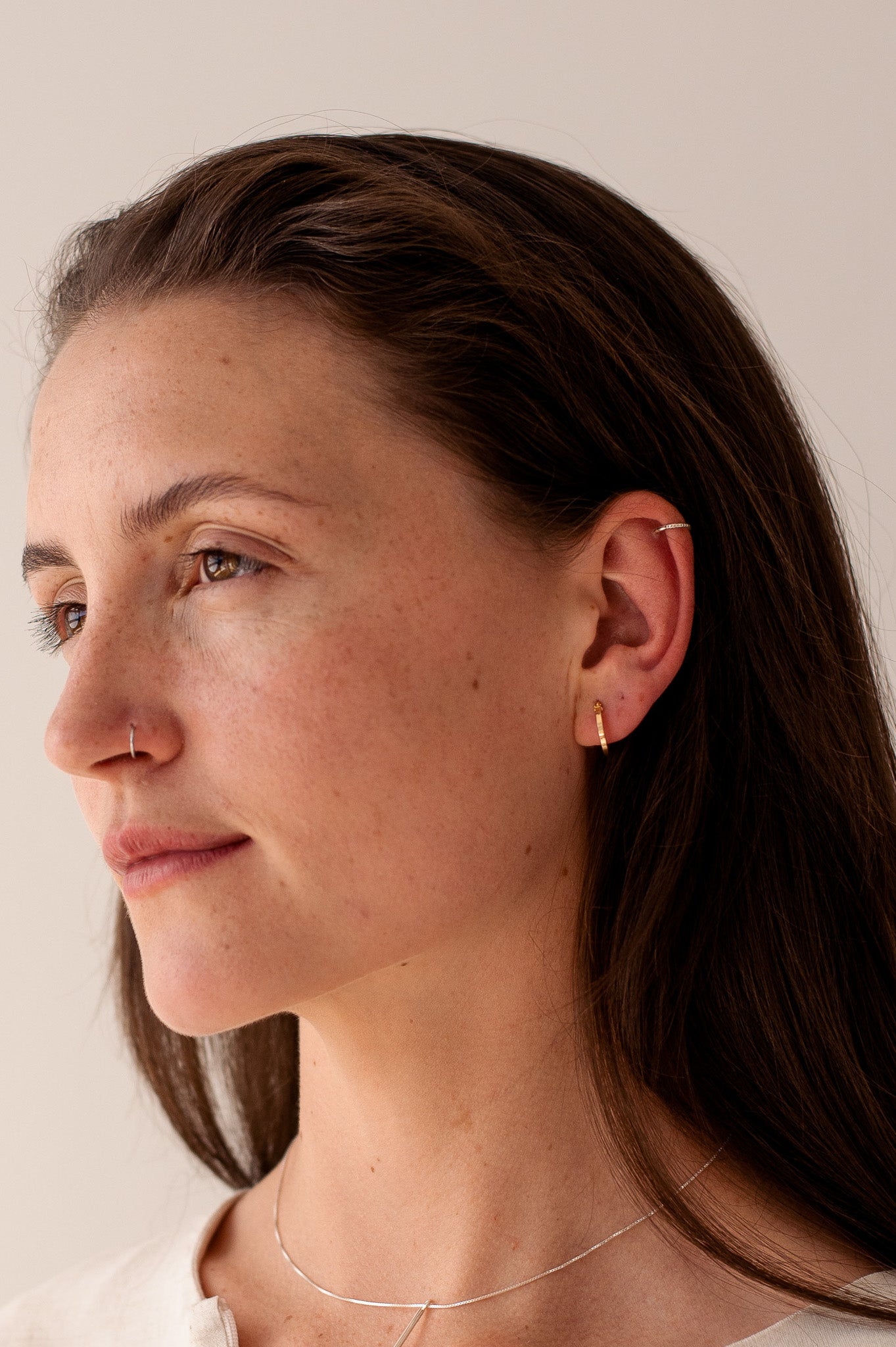 model wears minimalist jewellery. clean lines and little detail. model wears small hoops on earls and nose ring. model also wears thin chain 