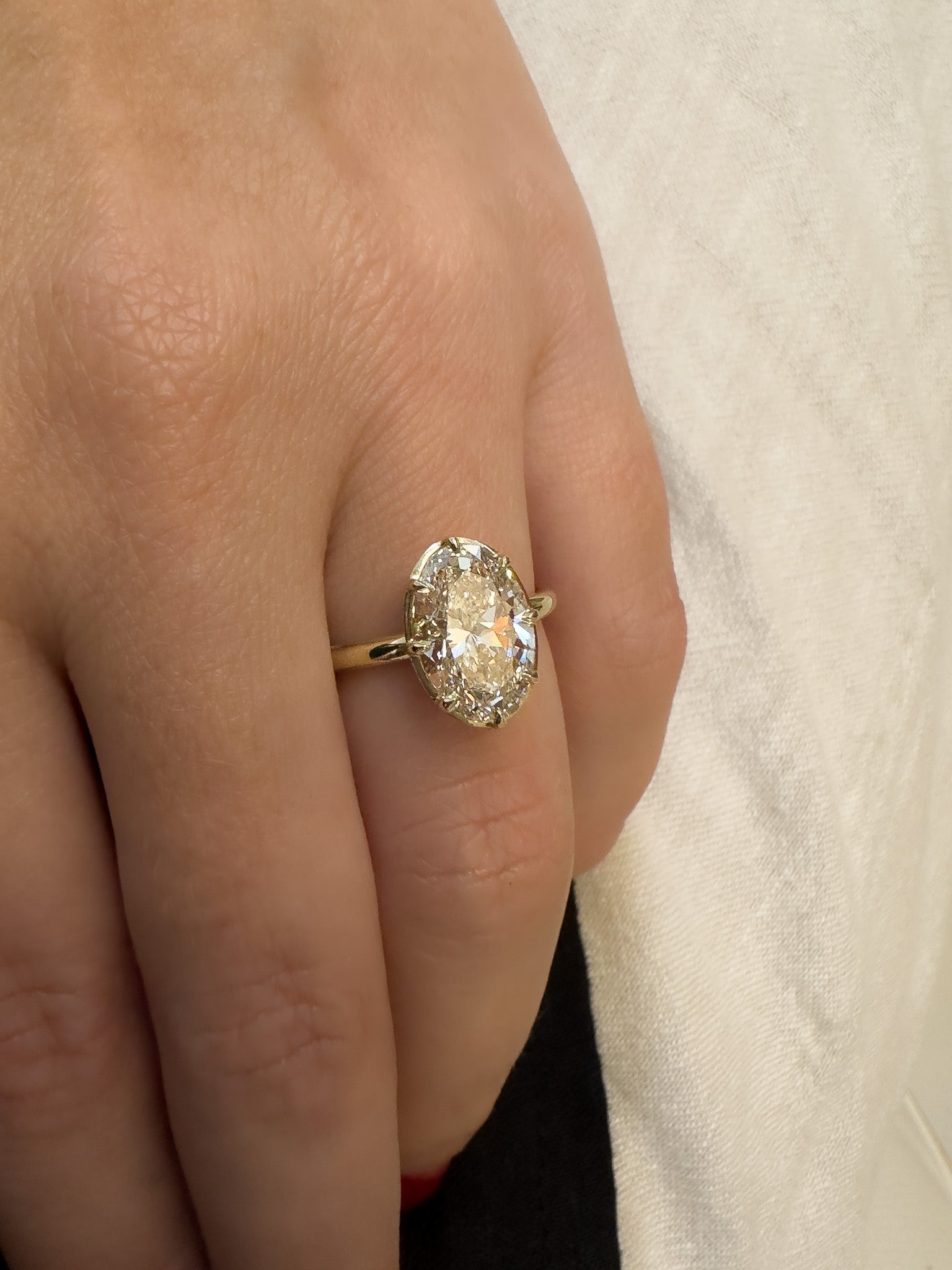 Gold ring with a diamond on a person's finger against a neutral background