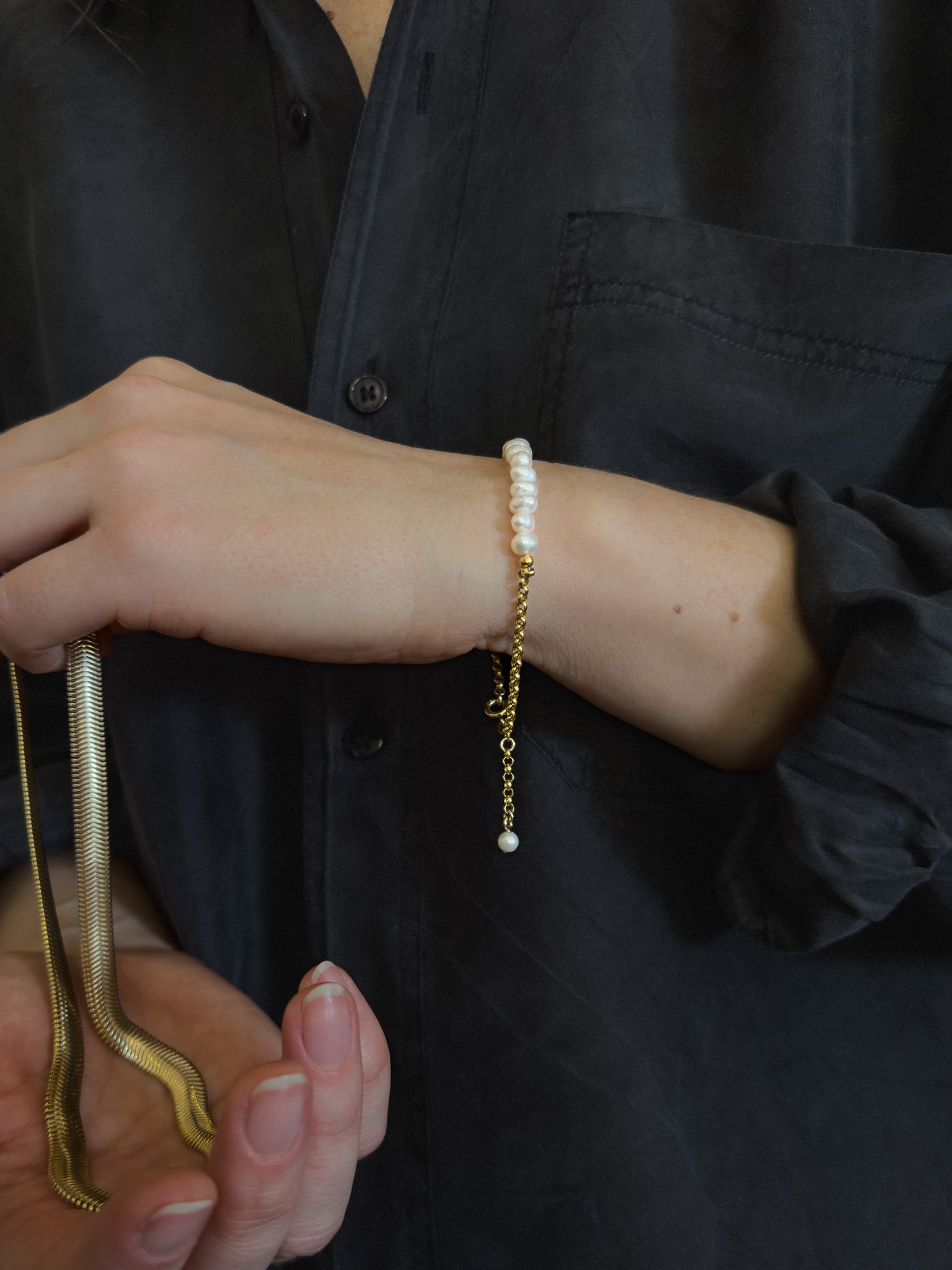 Model wears a pearl bracelet inn solid gold whist holding a luxurious snake chain necklace,