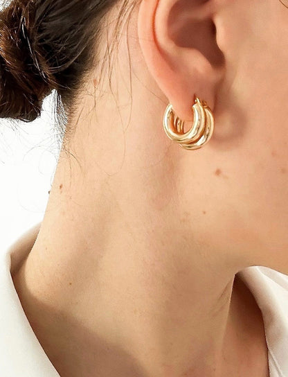 model wears multiple hoop earrings layered on one ear. 