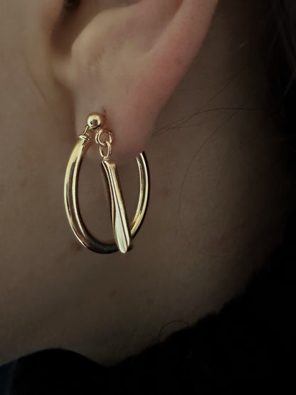 model wears solid gold hoop earrings with a swing stud earring for a multi earring look. layered earrings. two earring on one ear