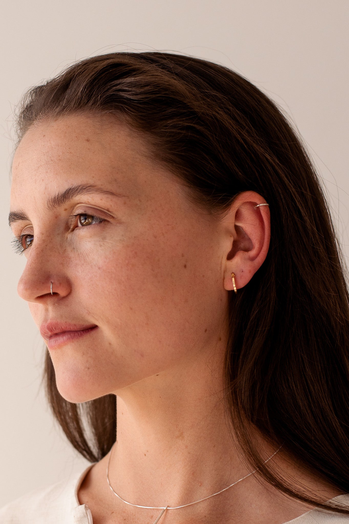 model wears minimalist jewellery. clean lines and little detail. model wears small hoops on earls and nose ring. model also wears thin chain