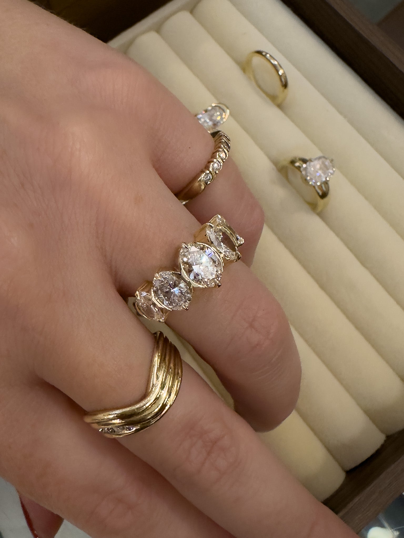 Gold ring with diamonds on a finger, with a jewelry box in the background