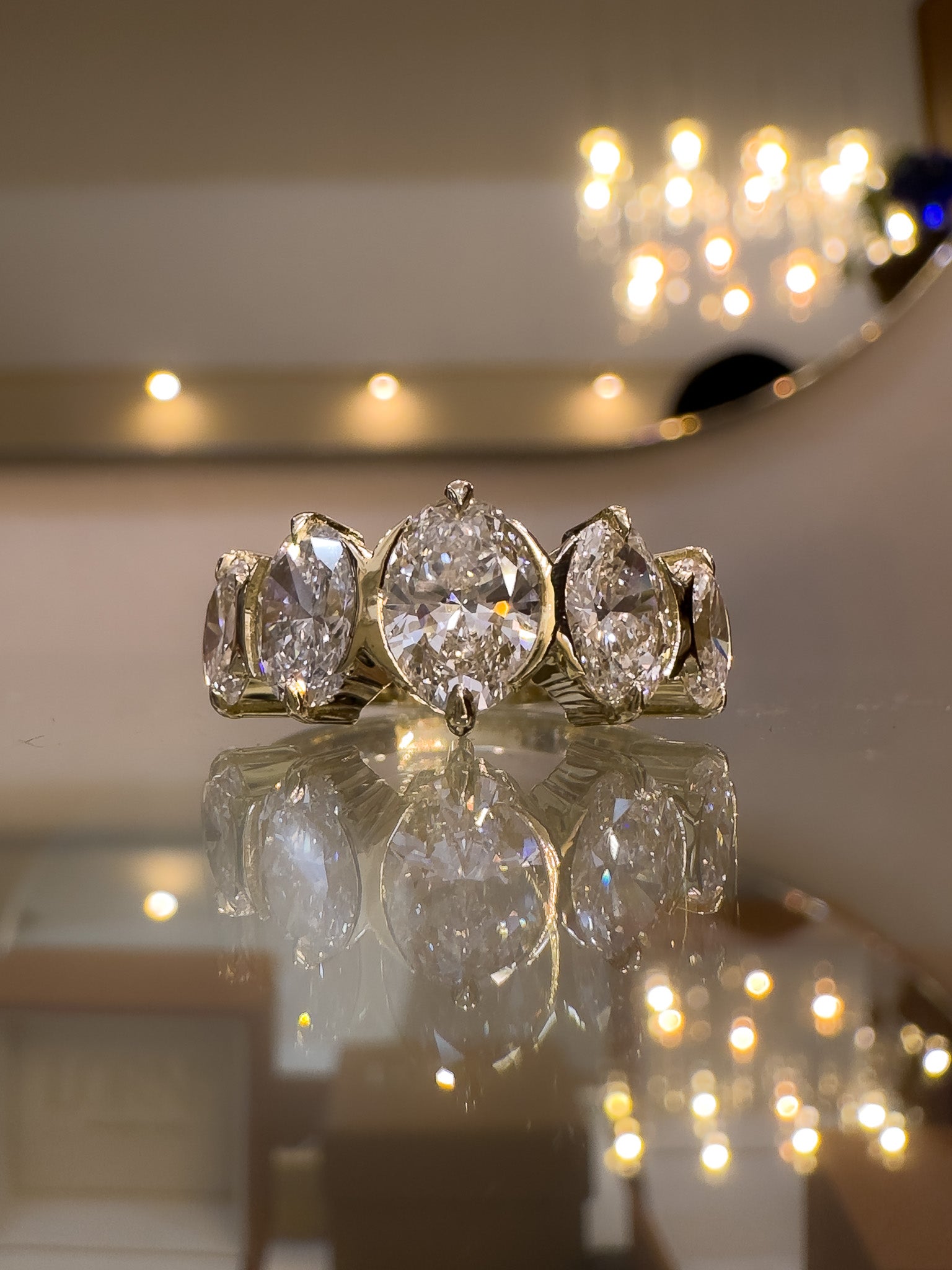 Diamond ring with three large gemstones on a reflective surface with blurred lights in the background