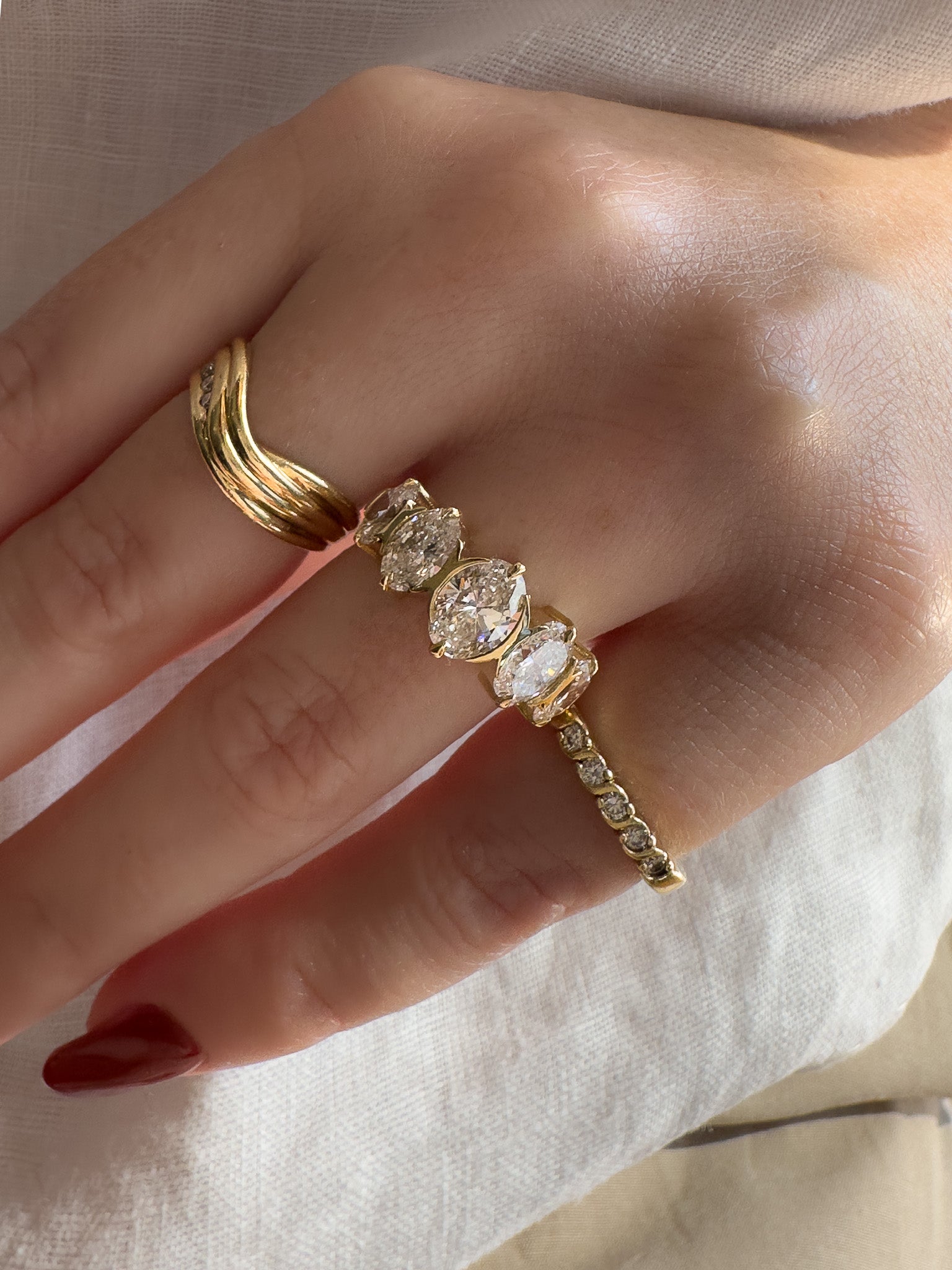 Hand wearing multiple gold rings with gemstones on a light background