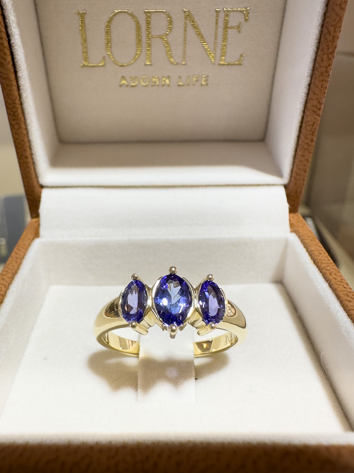 A gold ring with three oval-cut deep blue gemstones displayed inside an open Lorne jewelry box.