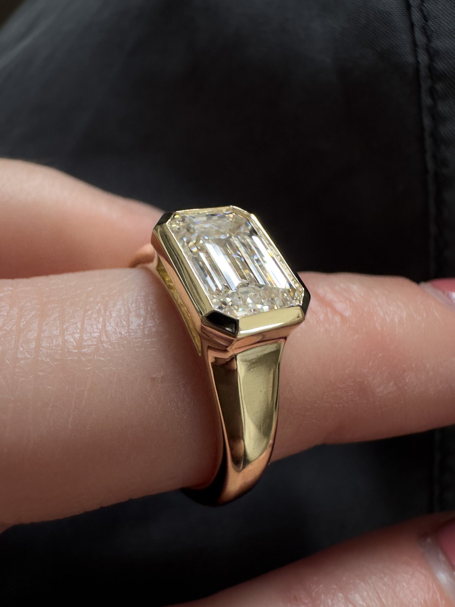 Gold ring with a diamond on a finger against a dark background