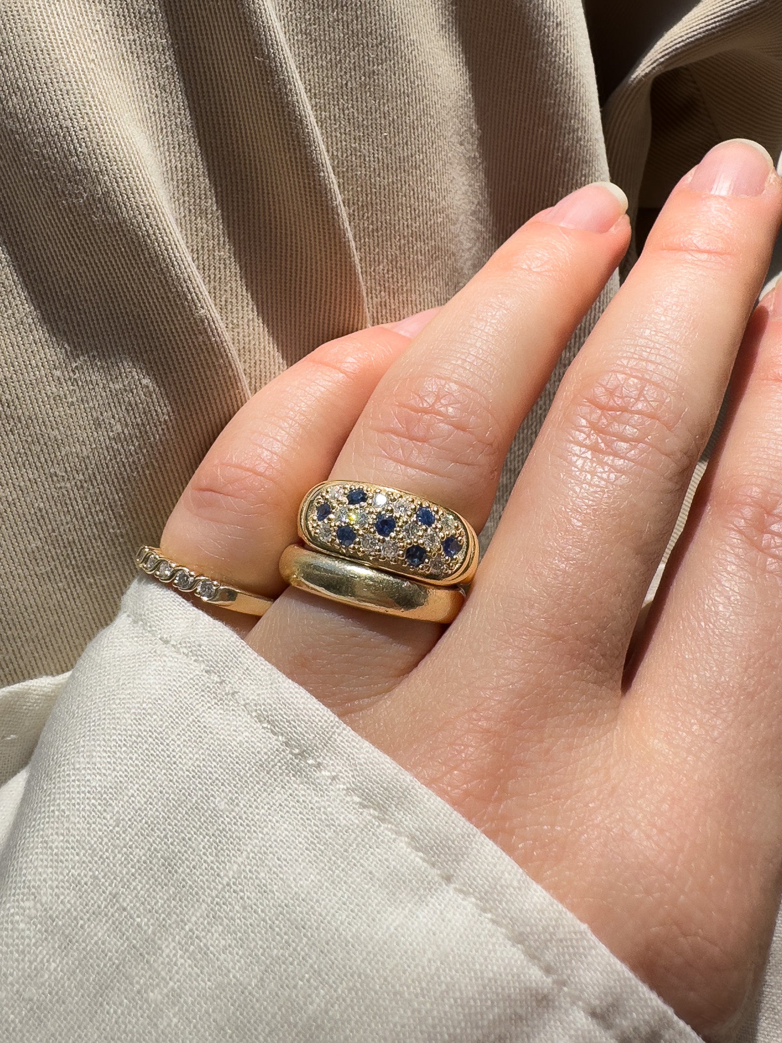Hand wearing two gold rings with gemstones against a beige fabric background