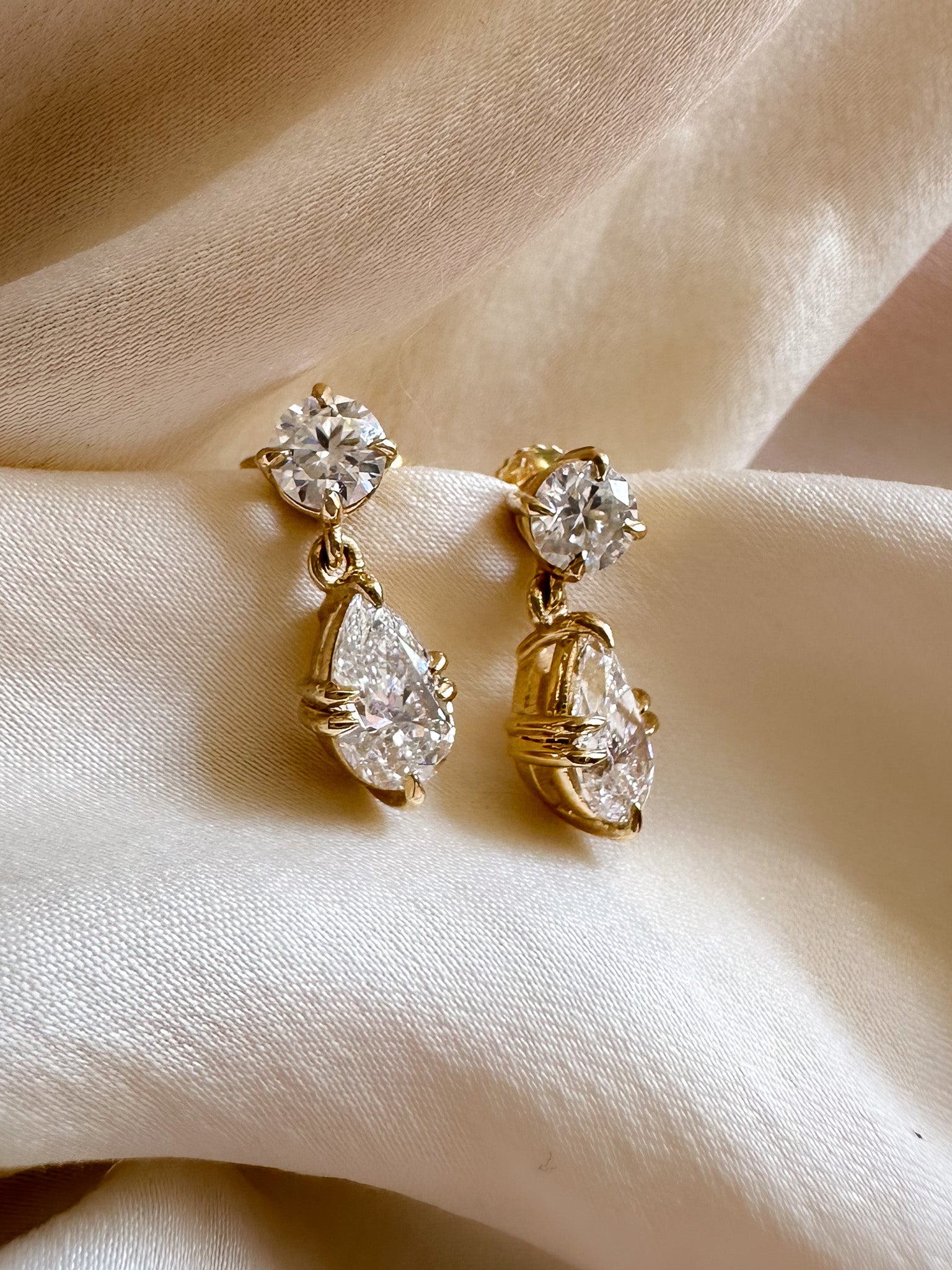 Gold earrings with clear gemstones on a beige fabric background