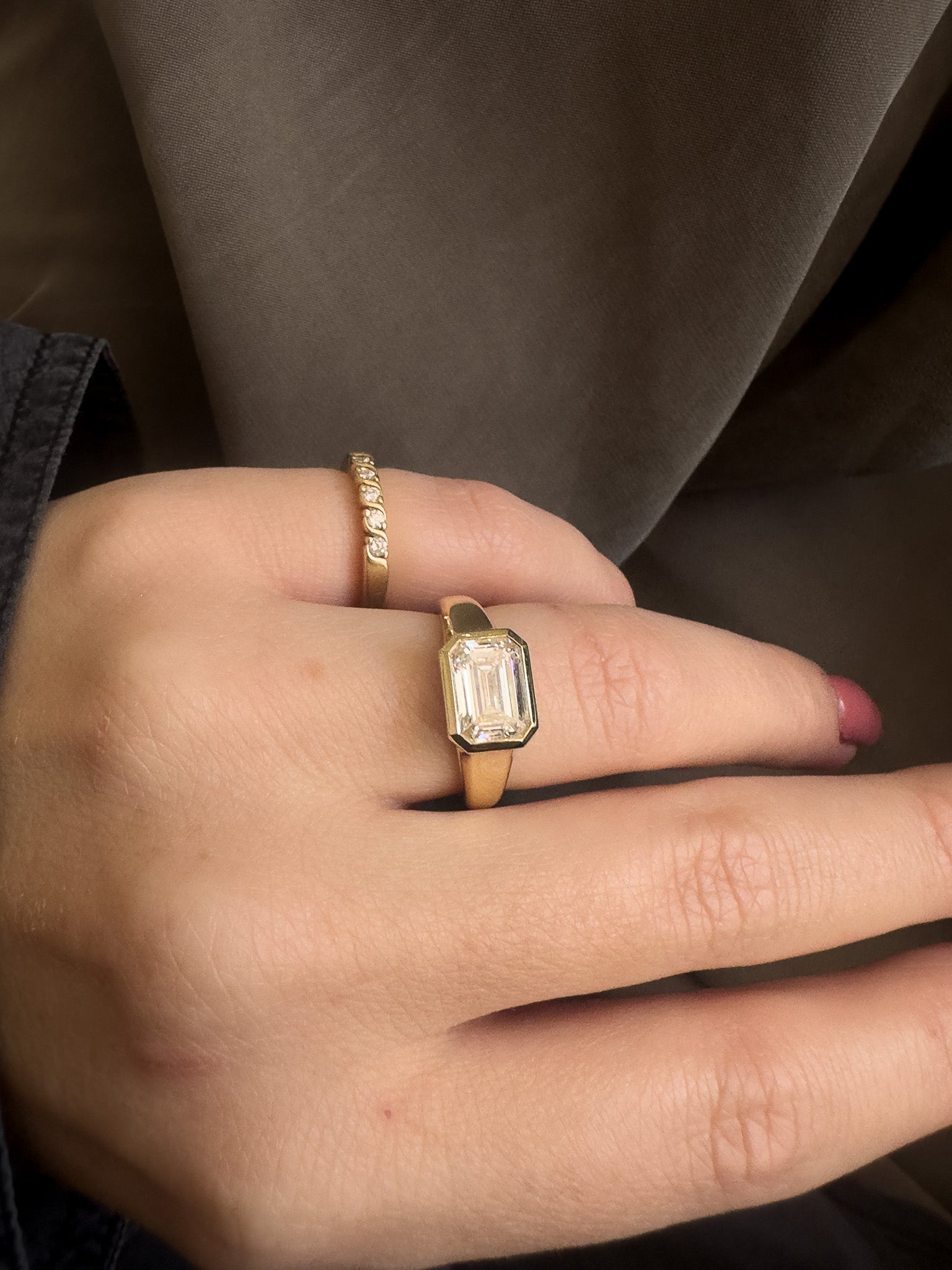 Gold ring with a diamond on a person's finger against a neutral background
