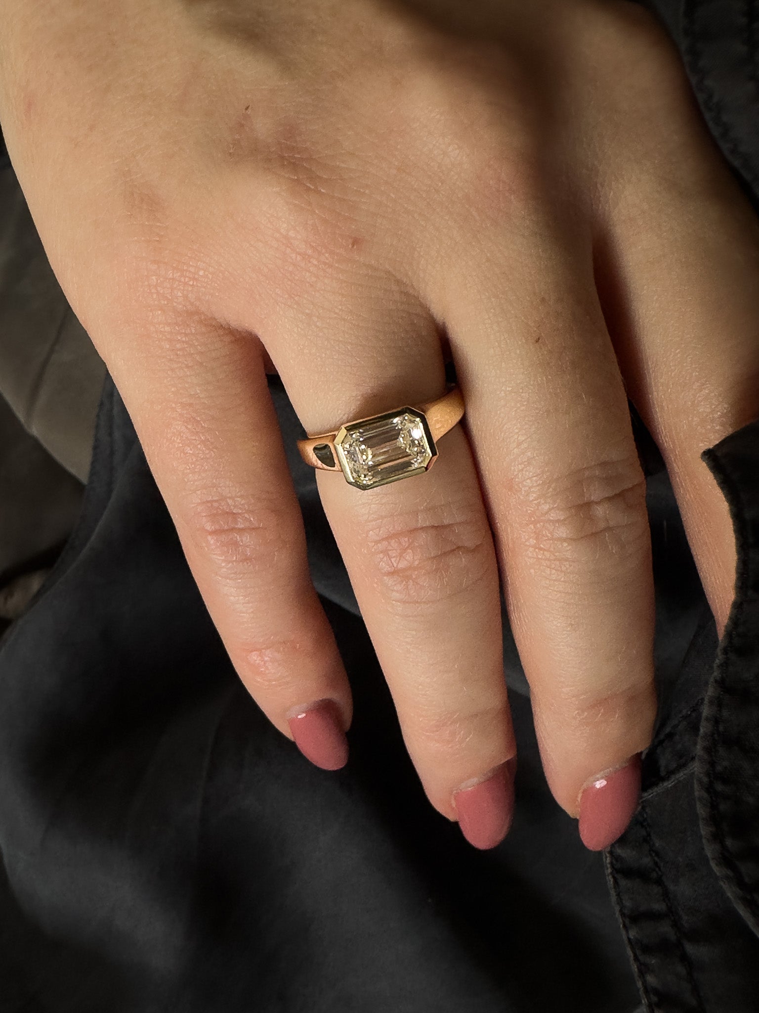 Close-up of a hand wearing a gold ring with a diamond on a dark background