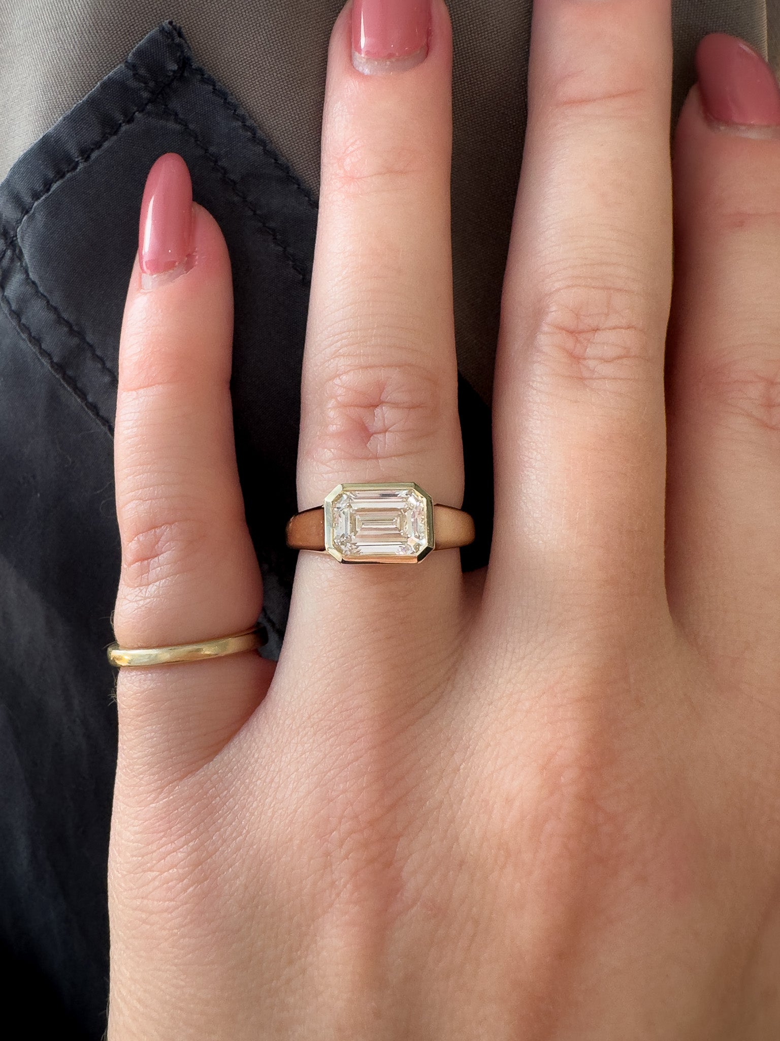 Hand wearing a gold ring with a diamond on a dark background