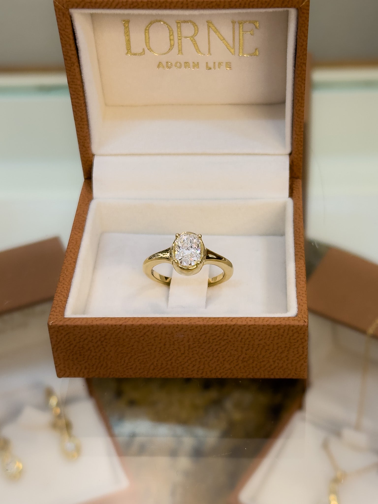 Gold ring with a diamond in an open brown jewelry box labeled 'LORNE'.
