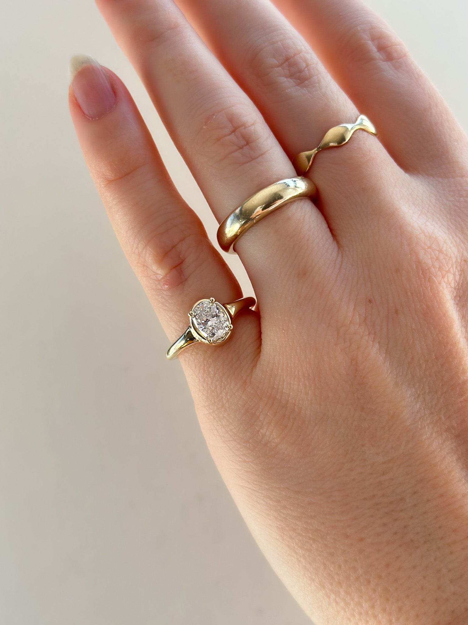Hand wearing two gold rings with a diamond on a plain background