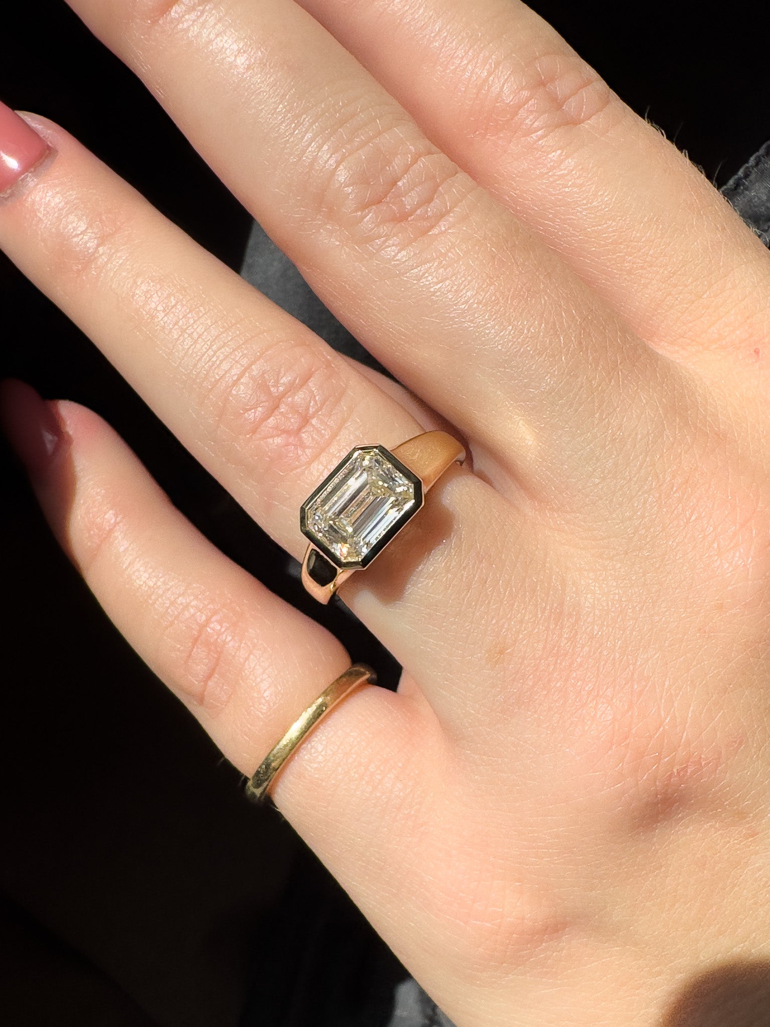 Close-up of a hand wearing a gold ring with a diamond on a dark background
