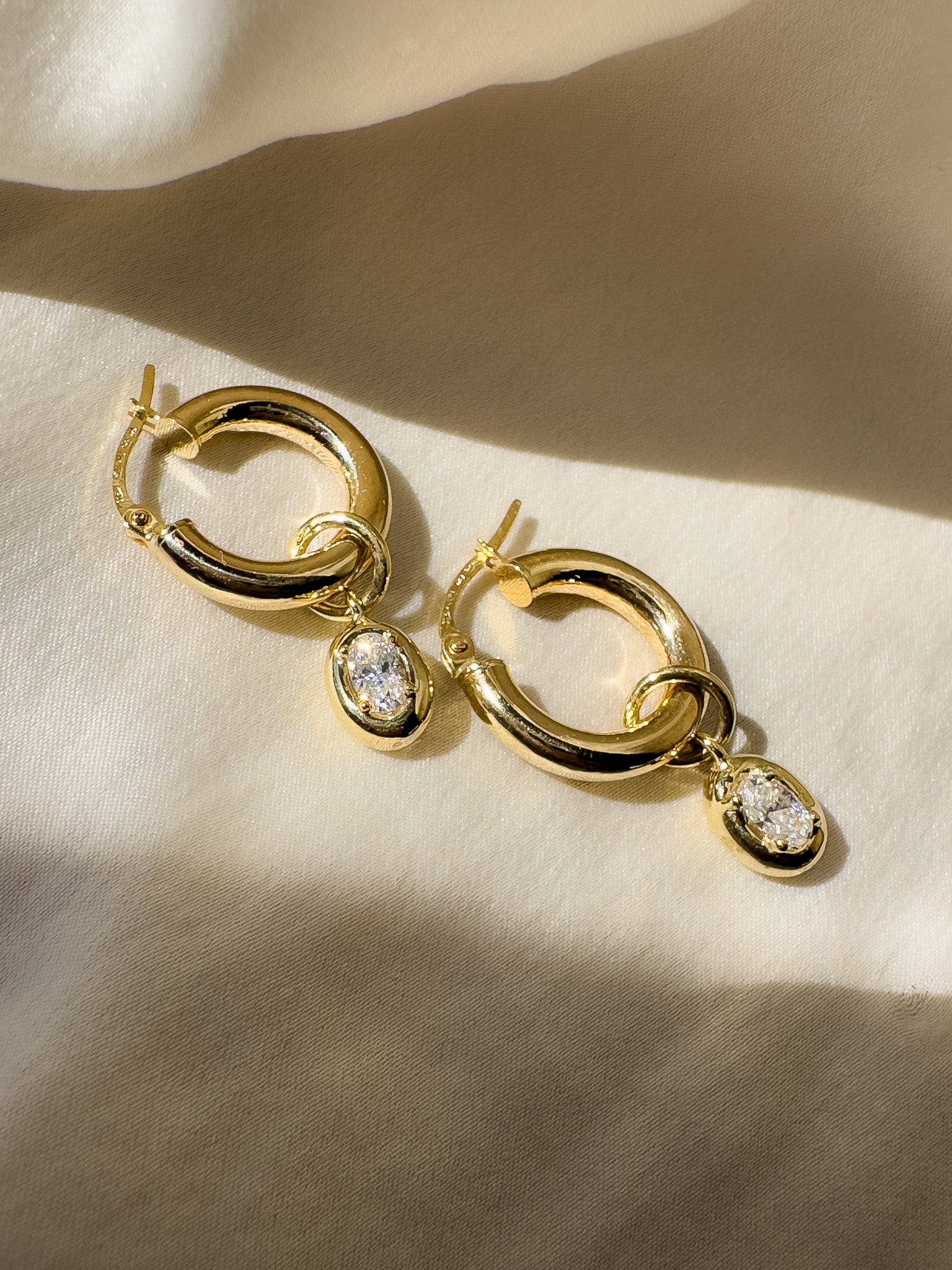 Gold hoop earrings with teardrop-shaped gemstones on a beige fabric background