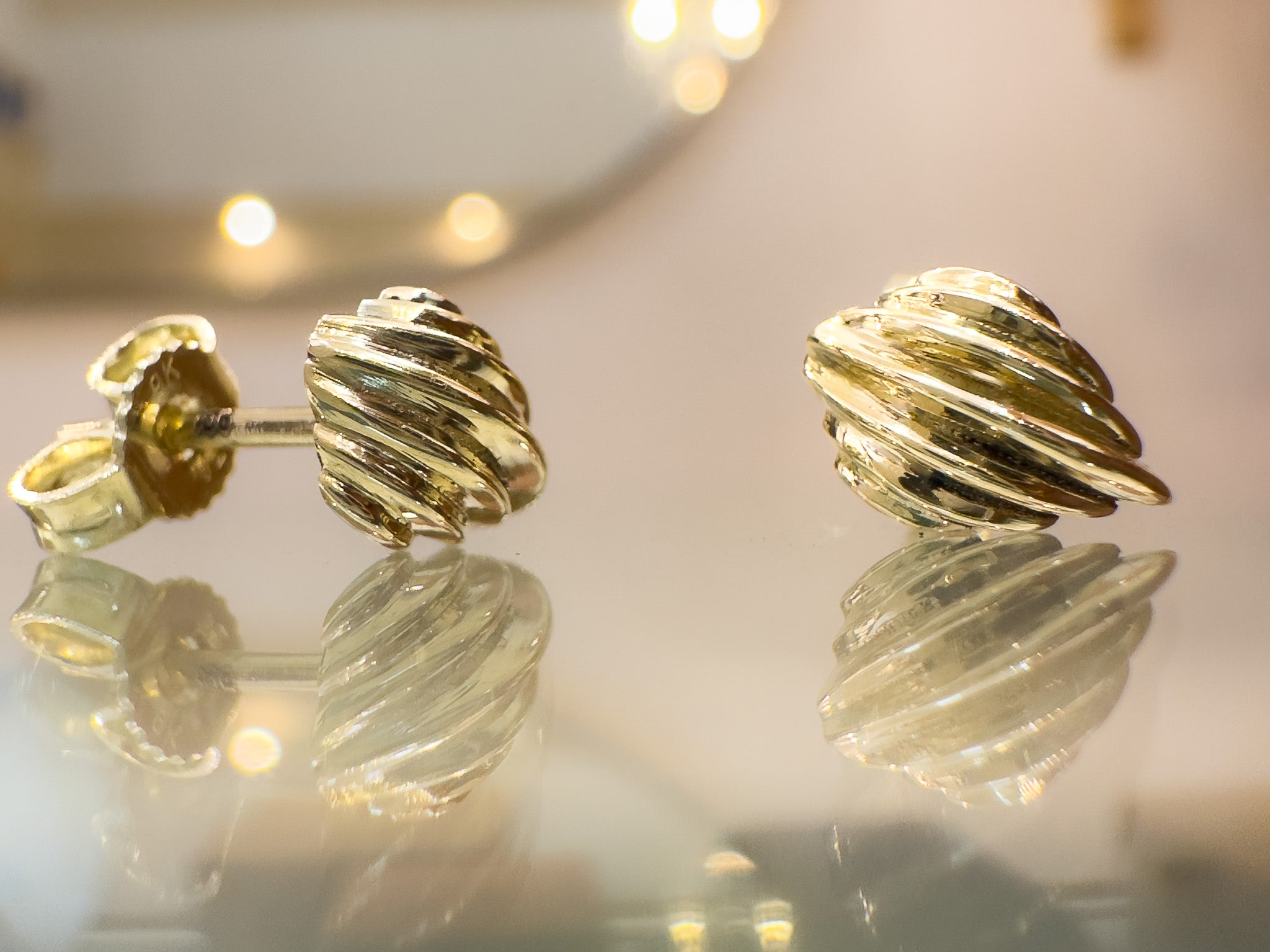 Gold earrings with a textured design on a reflective surface.