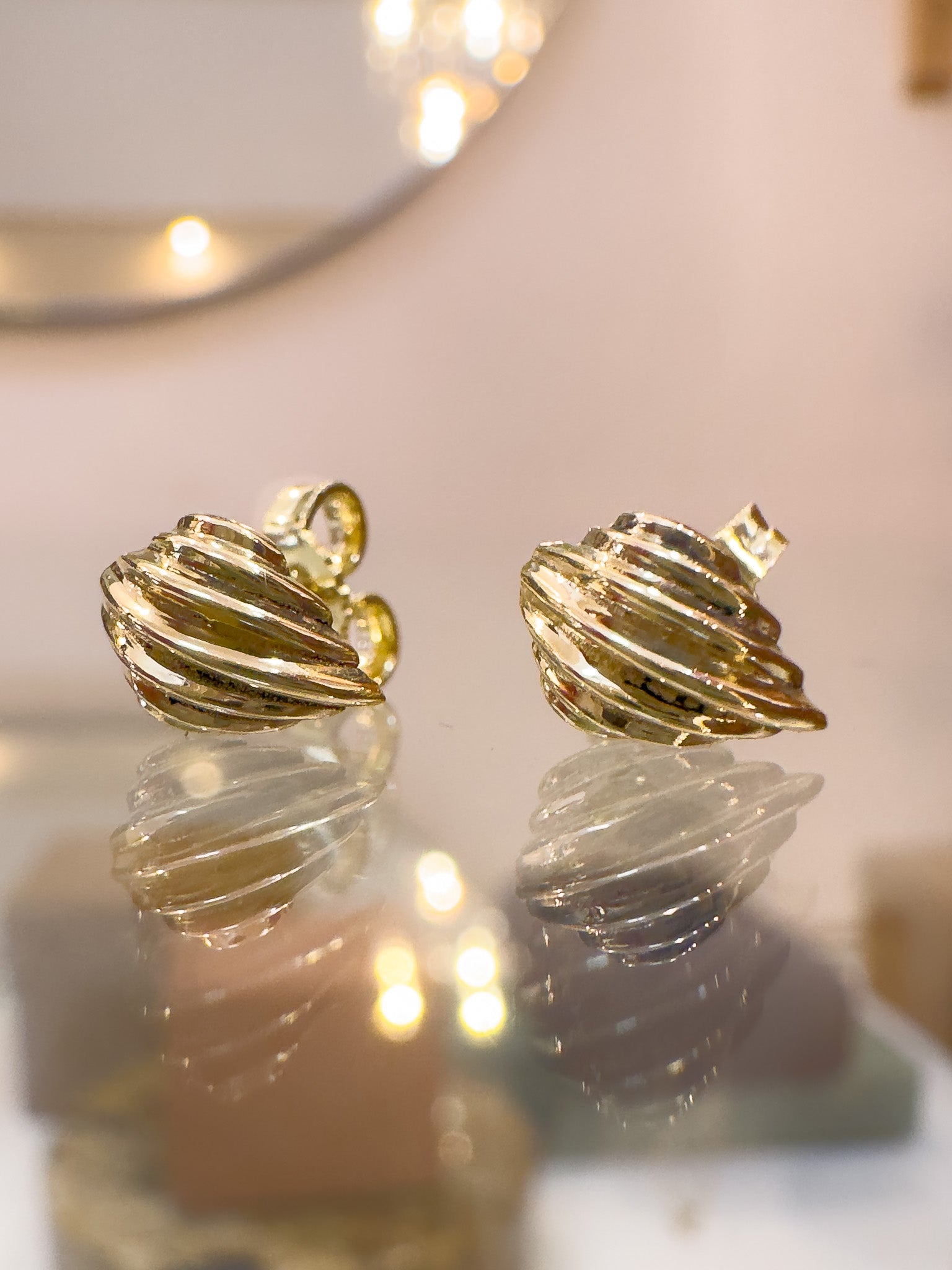 Gold spiral earrings on a reflective surface with blurred lights in the background