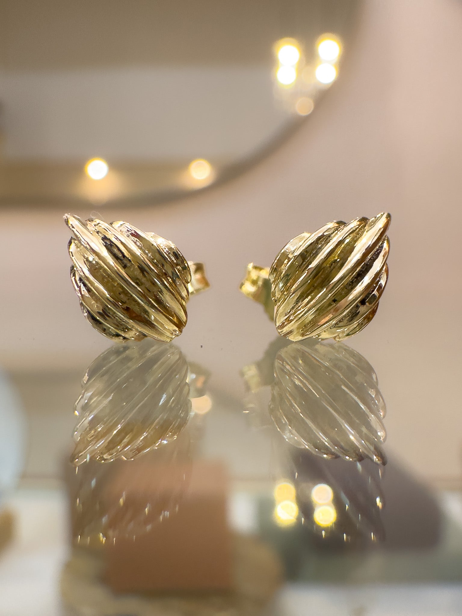 Gold leaf-shaped earrings on a reflective surface with a blurred background