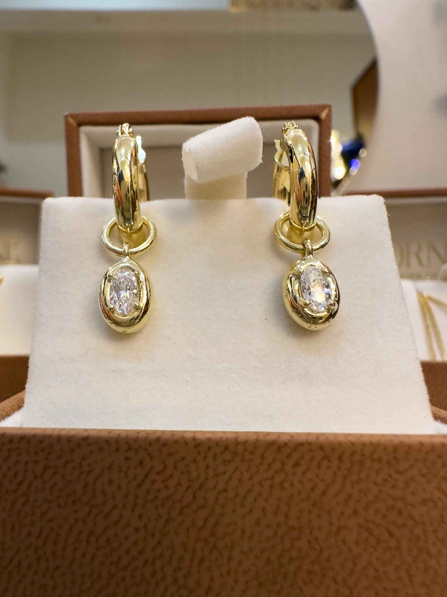 Gold hoop earrings with small round gemstones on a branded jewelry display box.