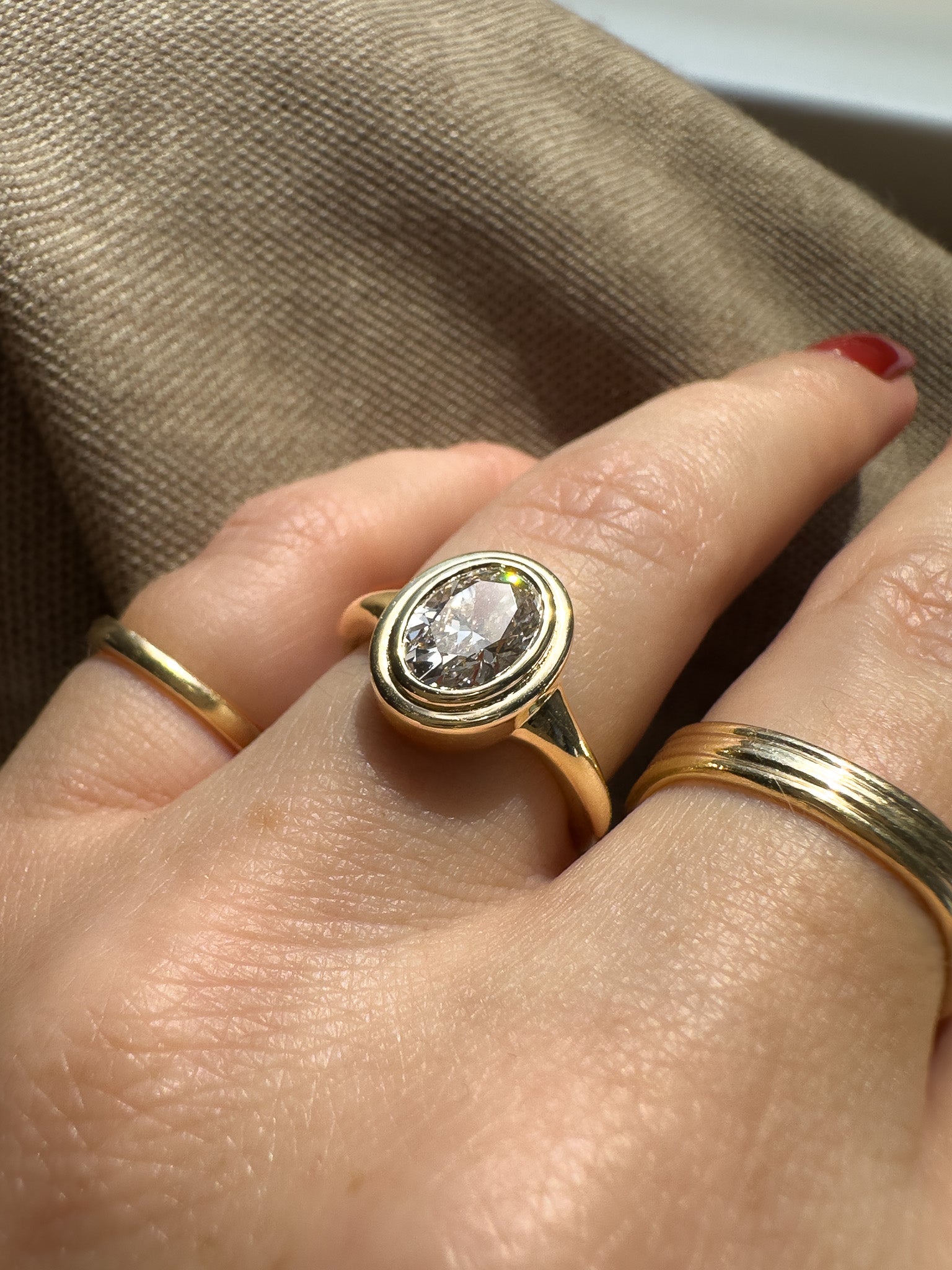 Gold ring with a diamond on a finger against a beige background
