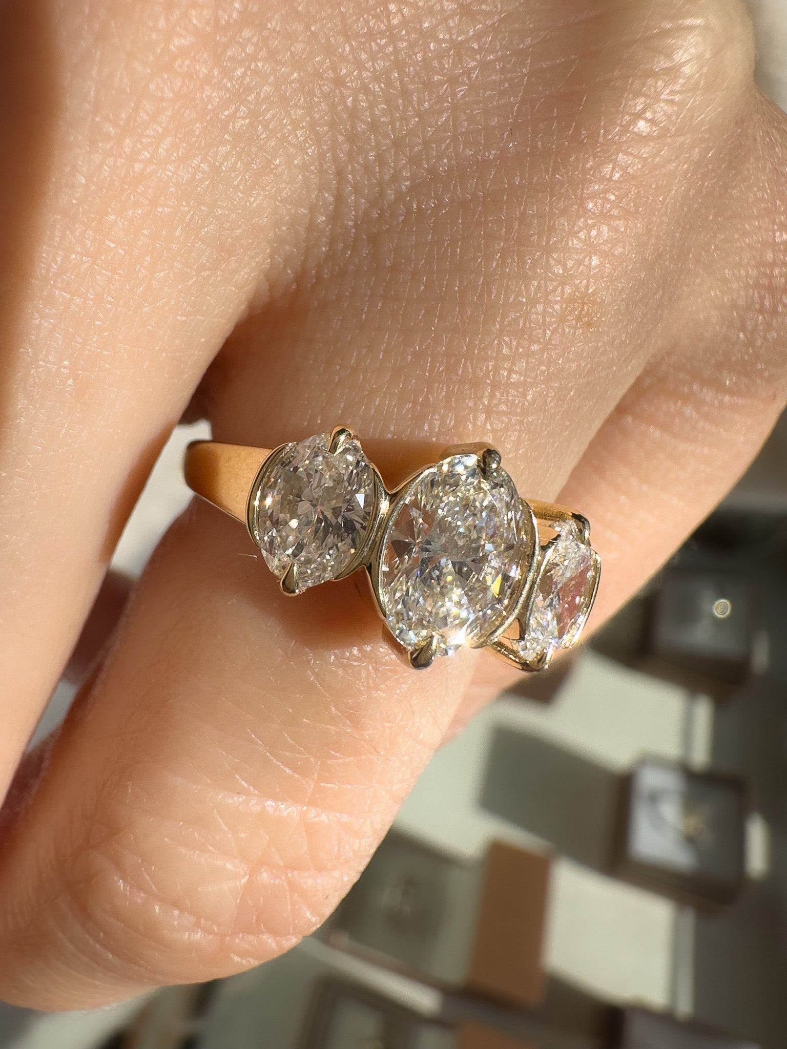 A close-up of a gold ring with three oval-cut clear gemstones worn on a finger. The center stone is oval, flanked by two marquise stones, set in a yellow gold band.