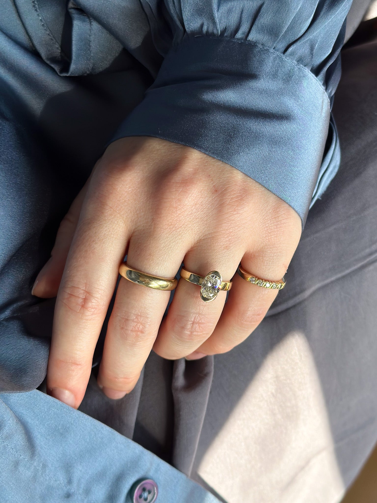 Close-up of a hand wearing two gold rings with a blue jacket sleeve.