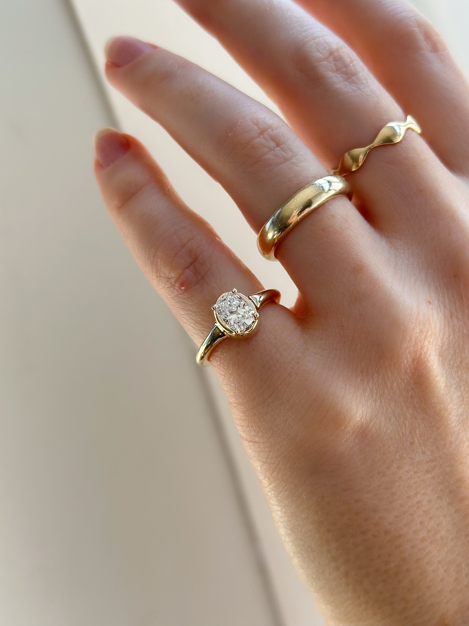 Hand wearing two gold rings with a diamond ring on a neutral background