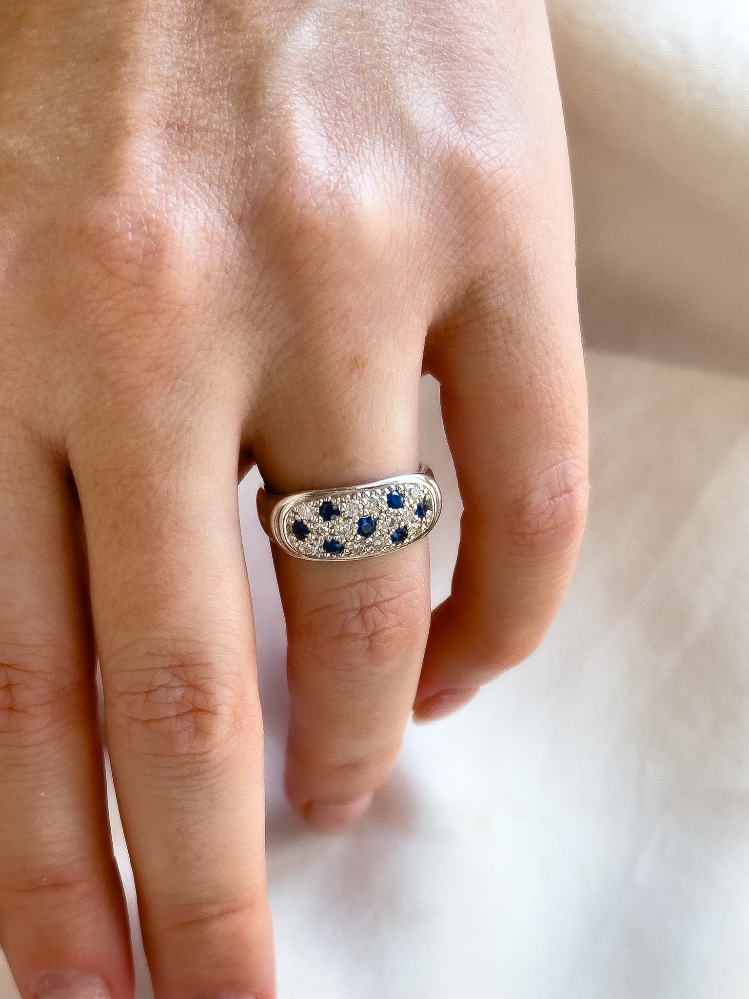 Silver ring with blue stones on a person's finger against a neutral background