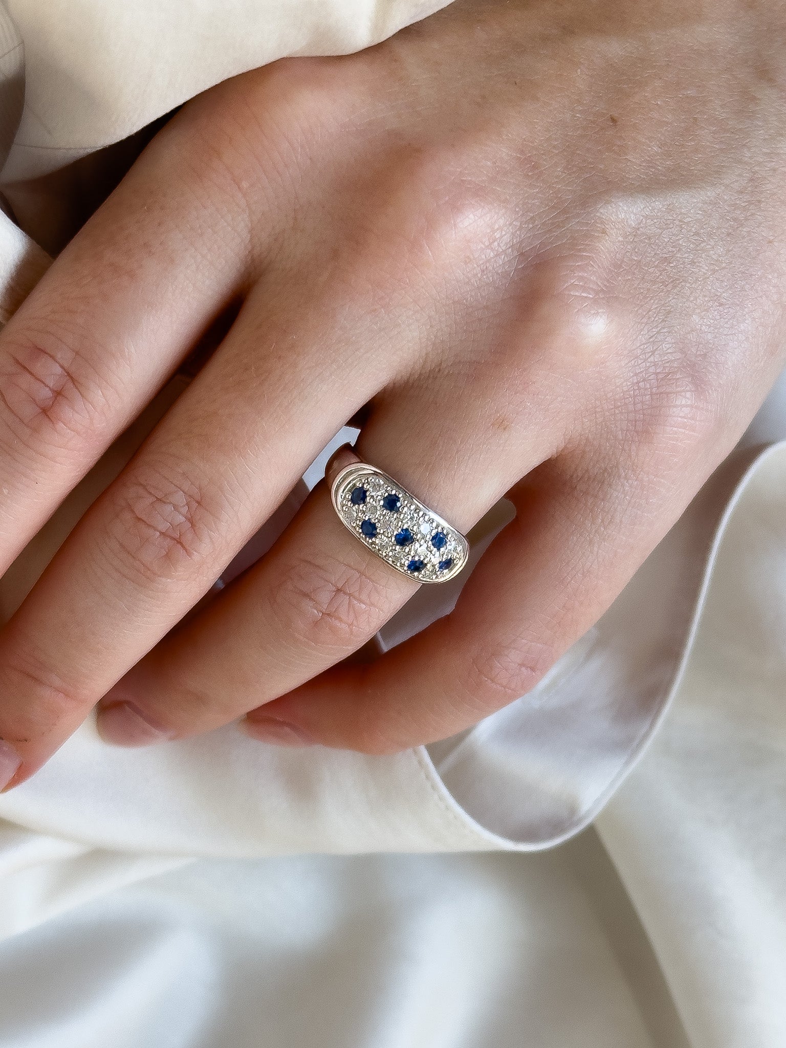 Close-up of a hand wearing a silver ring with blue stones on a white fabric background