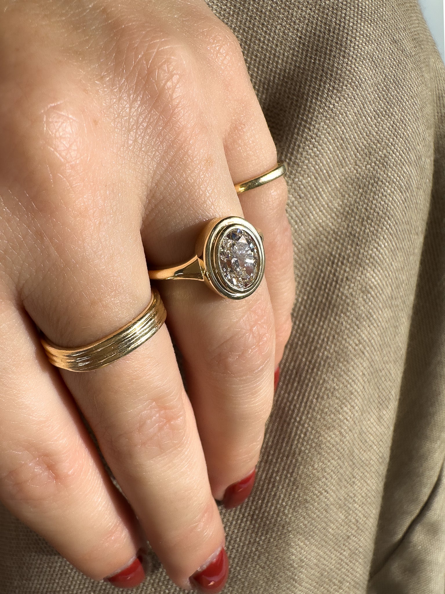Close-up of a hand wearing two gold rings with a diamond on a beige fabric background
