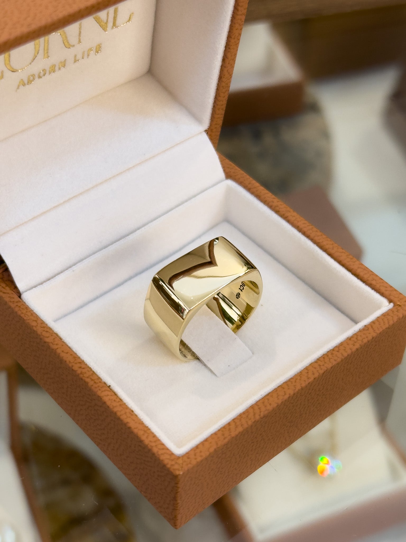 Gold signet ring in an open jewelry box with 'Adorn Life' branding.