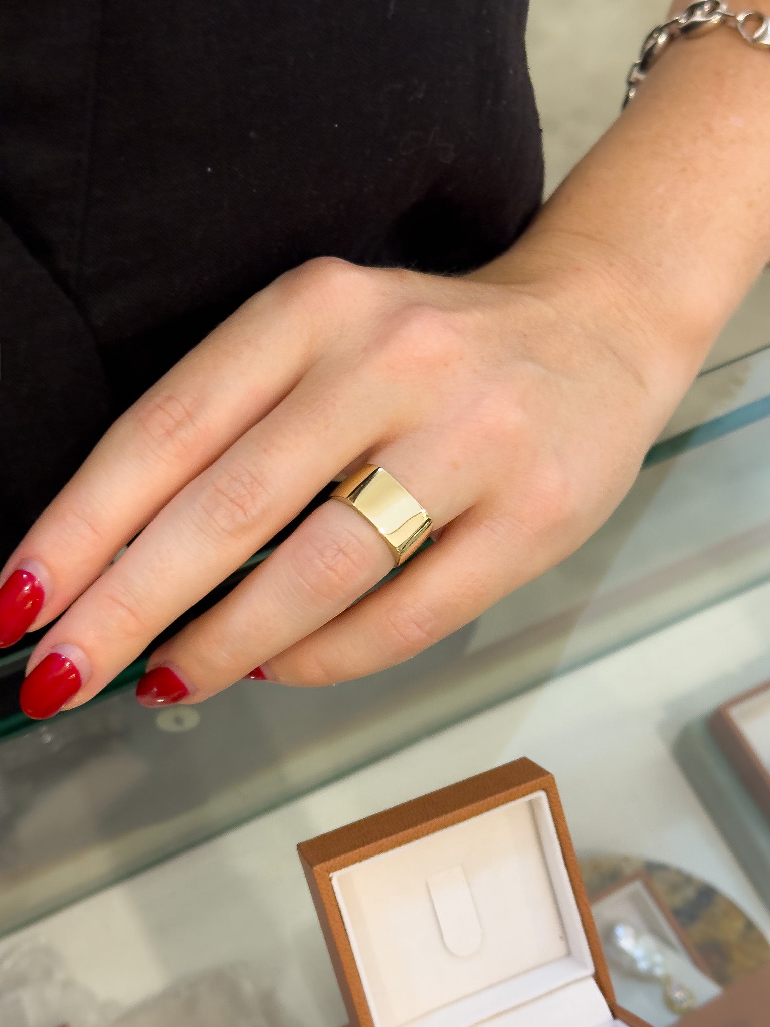 chunky Gold ring on a hand with red nail polish, next to an open jewelry box.