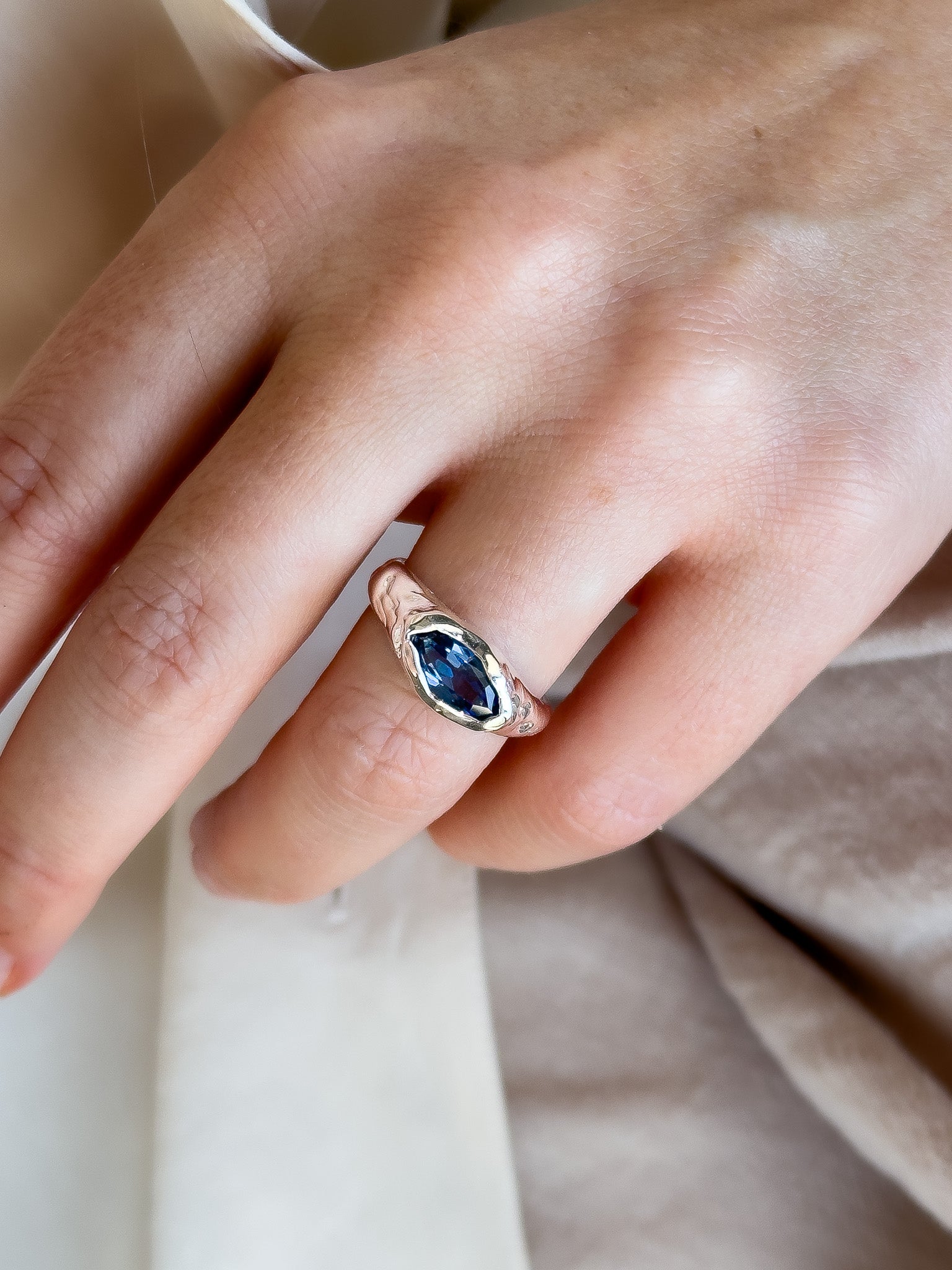 Close-up of a hand wearing a ring with a blue gemstone on a neutral background