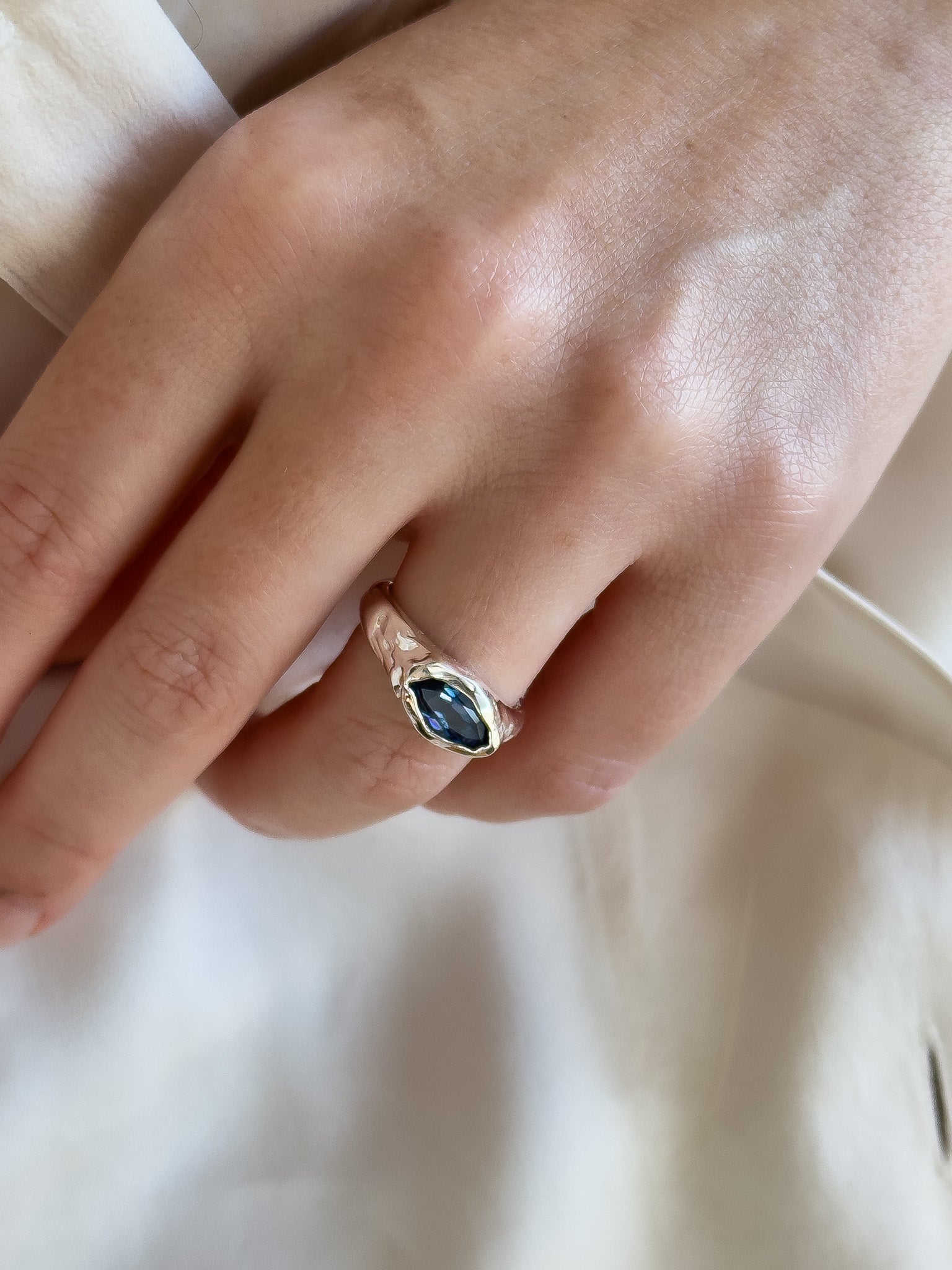 Close-up of a hand wearing a gold ring with a dark gemstone on a light background